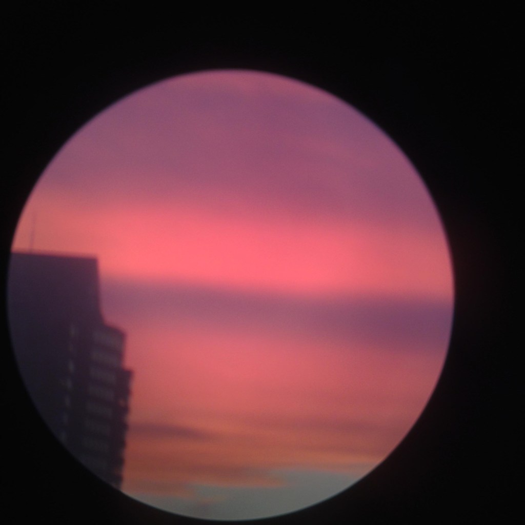 Digital image of a sunset sky with a building on the left. Taken on an iPhone 6, shot through monocular.