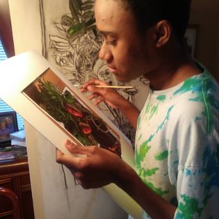 Malcolm Corley holding a paint brush in his right hand against a painting in progress that he holds up to his face with his left hand.